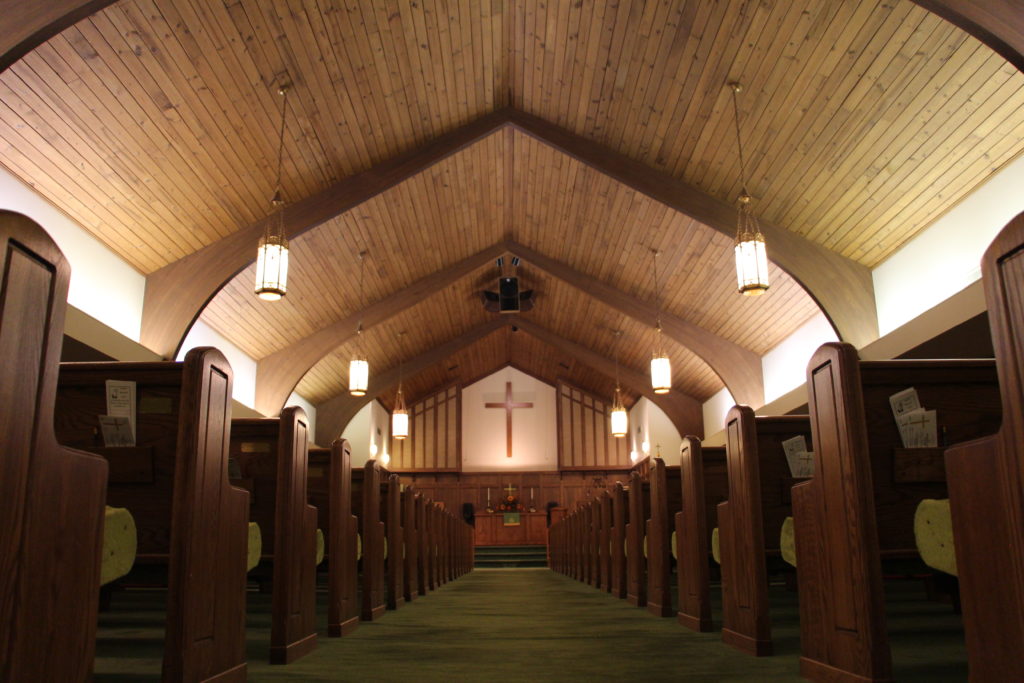 A view of a sanctuary from the back of the room looking down the center aisle with an altar and a cross as the focal points